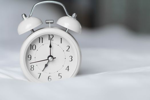 Alarm clock on white bad for wake up time with light from window, selective focus