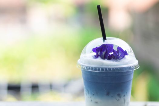 Closeup glass of ice butterfly pea latte on wood table with nature background