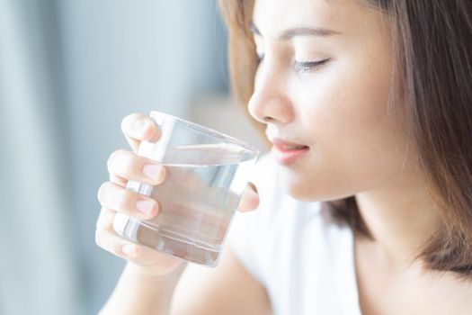 Close up woman drinking pure water from glass with light in the morning, Selective focus