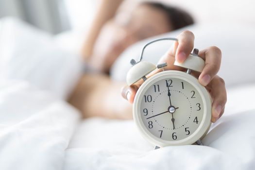 Closeup woman sleeping on bed and hand holding alarm on clock, Time to wake up