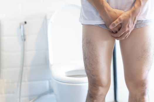 Closeup man holding bladder with pee pain in the toilet, selective focus