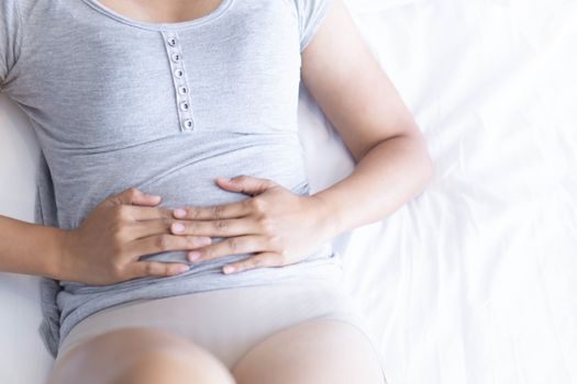 Close up woman stomachache lying on white bed, health care concept, selective focus