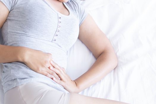 Close up woman stomachache lying on white bed, health care concept, selective focus