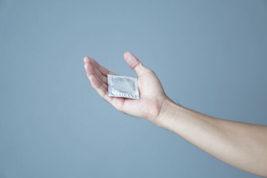 Close up man hand holding condom lying on white bed, health care and medical concept, selective focus