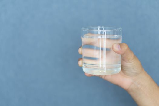 Close up woman hand holding a glass of pure water for dink with grey background, Health care concept