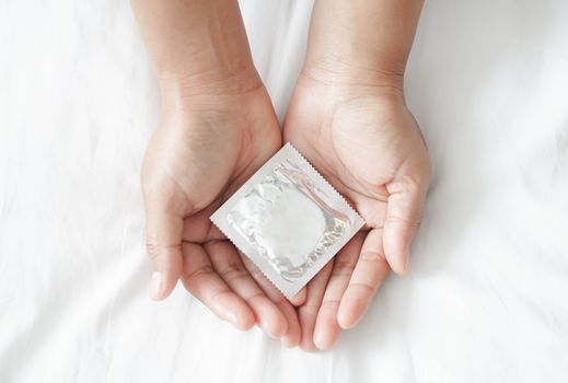 Close up woman hand holding condom lying on white bed, health care and medical concept