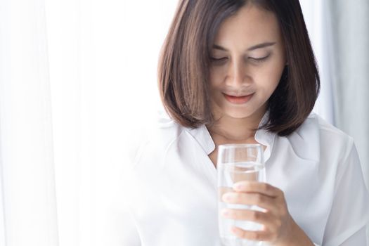 Close up woman drinking pure water from glass with light in the morning, Selective focus