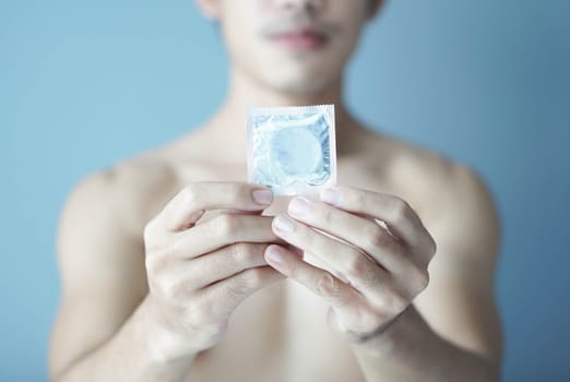 Close up man hand holding condom with blue background, health care and medical concept, selective focus