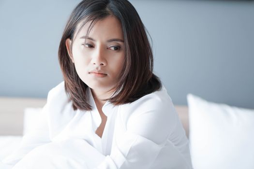 Closeup woman sitting on bed in the bedroom with thinking or depressed feeling, selective focus