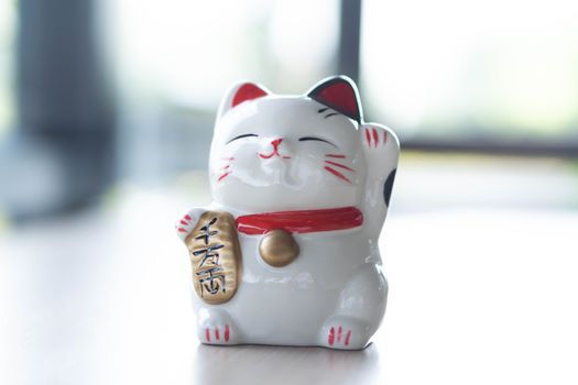 Maneki neko lucky cat show text on hand meaning rich on wood table background, select focus