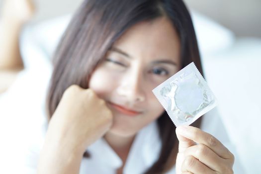 Close up woman hand holding condom with happy face lying on white bed, selective focus