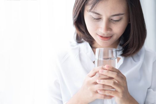 Close up woman drinking pure water from glass with light in the morning, Selective focus
