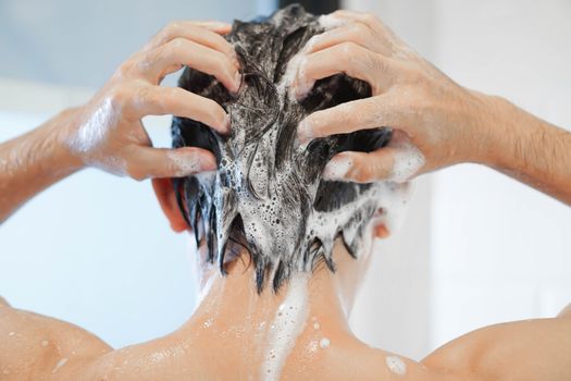 Closeup young man washing hair with with shampoo in the bathroom, vintage tone, selective focus