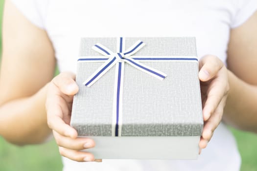 Woman hand holding grey gift box  on green nature background