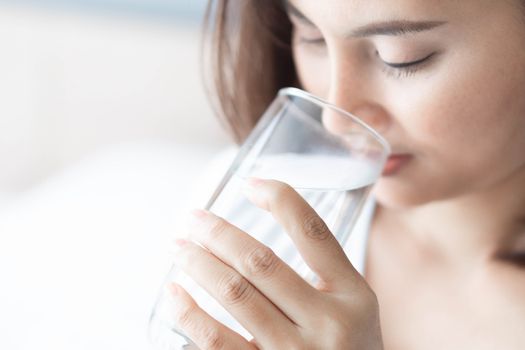 Close up woman drinking pure water from glass with light in the morning, Selective focus