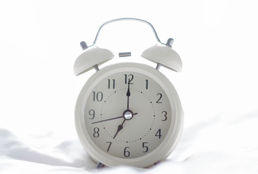 Alarm clock on white bad for wake up time with light from window, selective focus