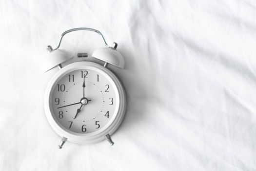Alarm clock on white bad for wake up time with light from window, selective focus
