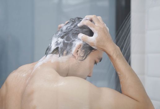 Closeup young man washing hair with with shampoo in the bathroom, vintage tone, selective focus