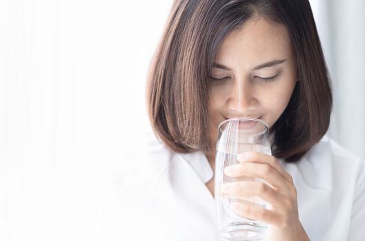 Close up woman drinking pure water from glass with light in the morning, Selective focus