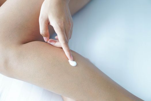 Woman hand applying cream or lotion on leg lying on white bed, selective focus