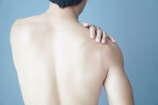 Closeup man hand holding shoulder with pain on blue background, health care and medical concept