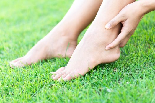 Woman hand holding foot with pain on green grass nature background, health care and medical concept