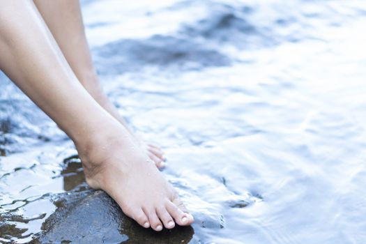 Woman legs relaxing with water on stone in the river for relax feeling