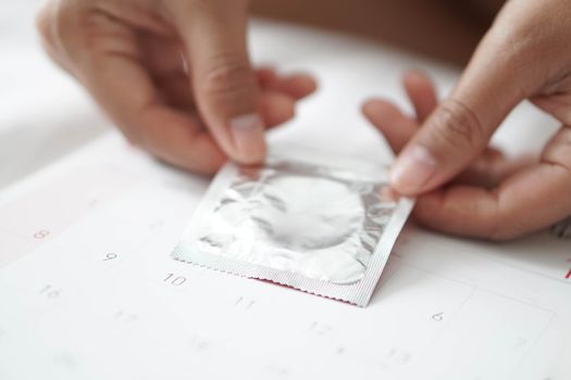 Close up woman hand holding condom  on calendar background, health care concept, selective focus