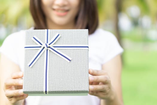 Woman hand holding grey gift box  on green nature background