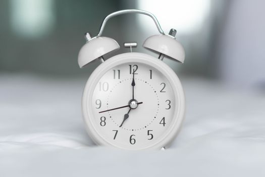 Alarm clock on white bad for wake up time with light from window, selective focus