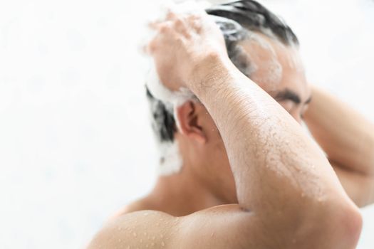 Closeup young man washing hair with with shampoo in the bathroom, health care concept, selective focus