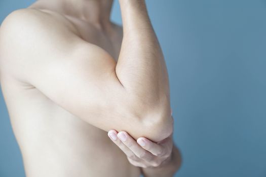Closeup man hand holding elbow with pain with blue background, health care and medical concept