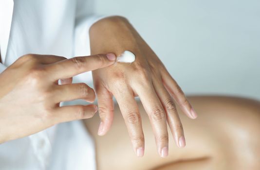 Woman hand applying cream or lotion on hand lying on white bed, selective focus