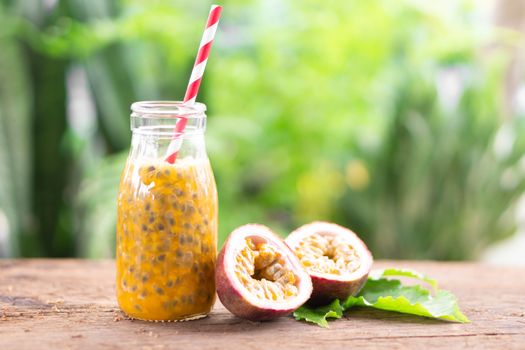 Glass bottle of passion fruit juice wood table with green nature background, food healthy concept