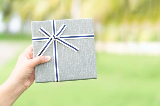 Woman hand holding grey gift box  on green nature background
