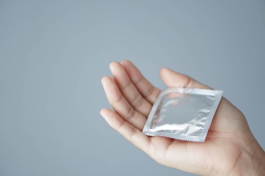 Close up woman hand holding condom lying on white bed, health care and medical concept