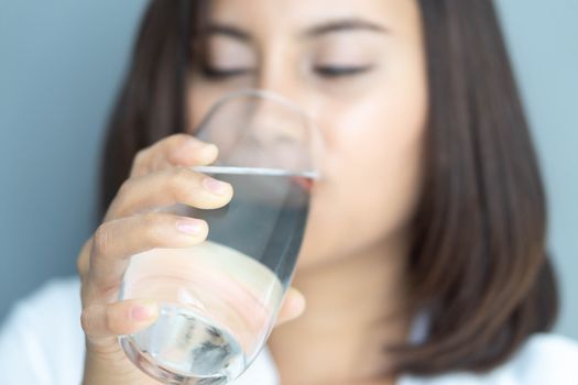 Close up woman drinking pure water from glass with blue background, Selective focus