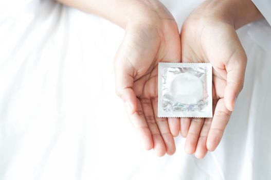 Close up woman hand holding condom lying on white bed, health care and medical concept