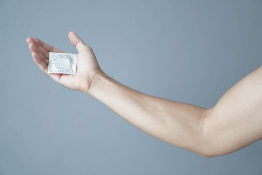 Close up man hand holding condom with grey background, health care and medical concept