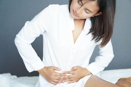 Close up woman stomachache lying on white bed, health care concept, selective focus