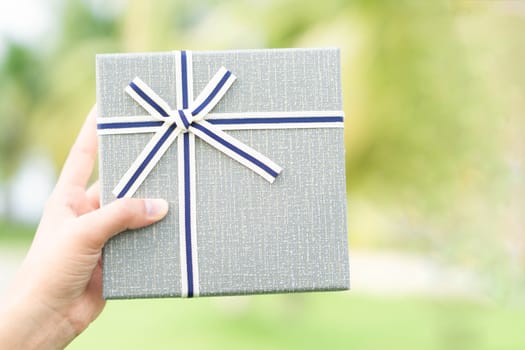 Woman hand holding grey gift box  on green nature background