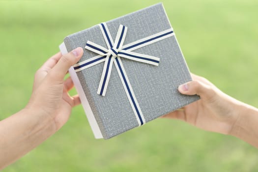 Woman hand holding grey gift box  on green nature background