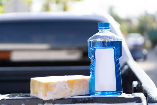 Close up bottle of car wash soap with yellow sponge for washing, selective focus