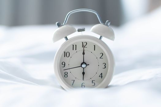 Alarm clock on white bad with light from window, selective focus