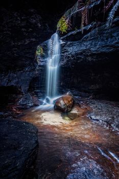 Waterfall tumbles over rock in a remote small dark canyon in Blue Mountains Australia