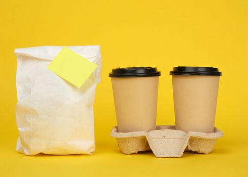 white paper bag, brown paper disposable cups with a plastic lid stand in the tray on a yellow background, takeaway containers