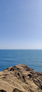 Vertical landscape of onlooking blue ocean from a rocky dusty cliff in daylight in jeju Island, South Korea