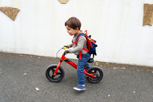 Little boy rides his red balance bike on a pavement, with some motion blur