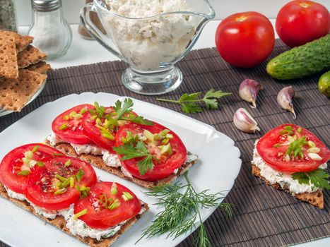 Crispy bread from buckwheat flour smeared with curd cheese on top a tomato with greens and spices is shown close up