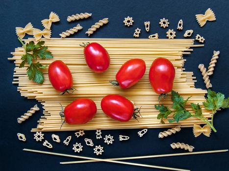 Spaghetti with tomatoes, greens and other figured pasta in the form of bows, spirals, figures of rockets and stars for cooking on a dark background